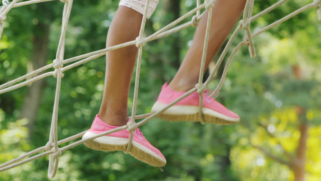 pies de un niño afroamericano caminando por un cable estirado entre árboles