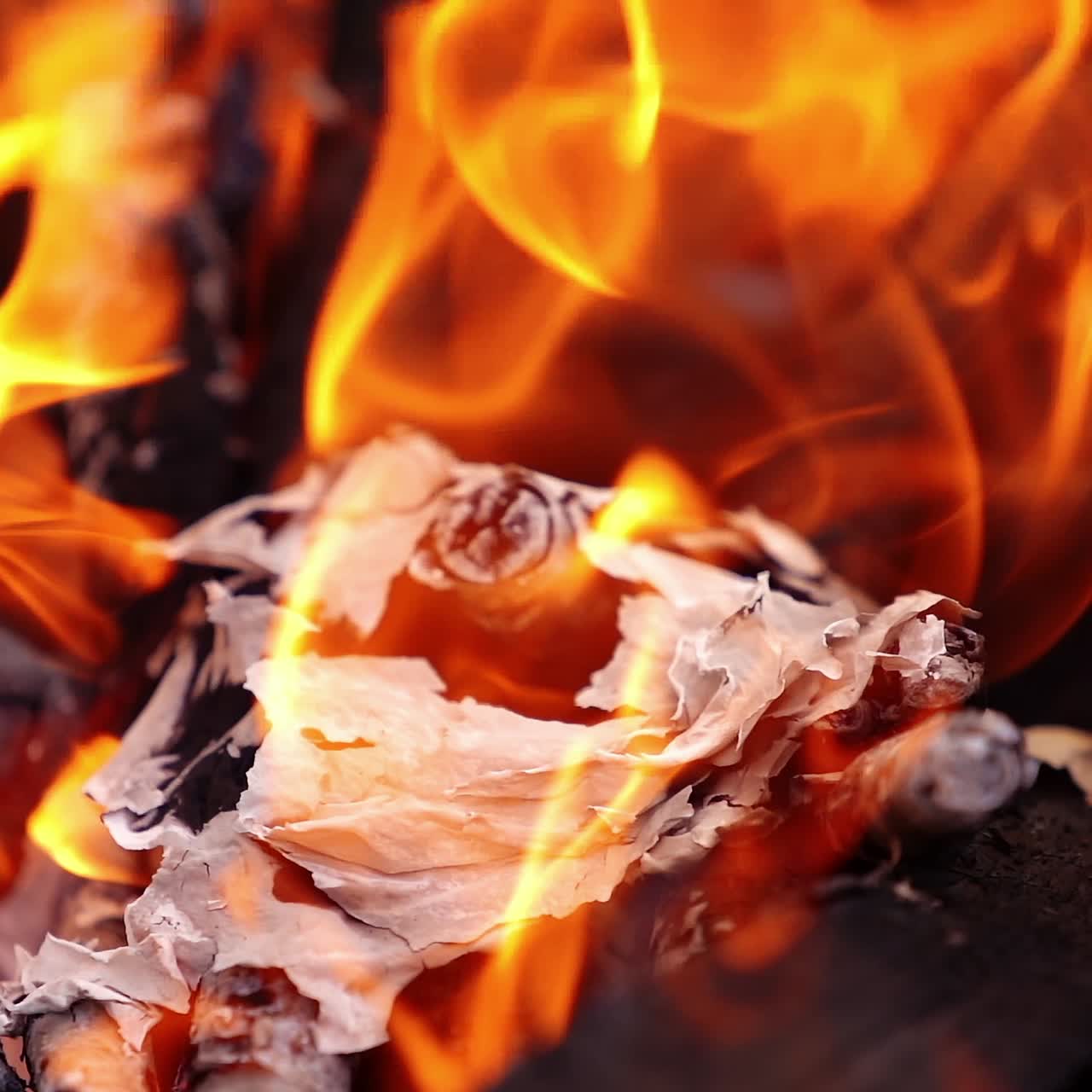 Embers of paper in fire. Bright orange flame on smoldering logs. Dancing of fire flame. Close-up. Slow motion.