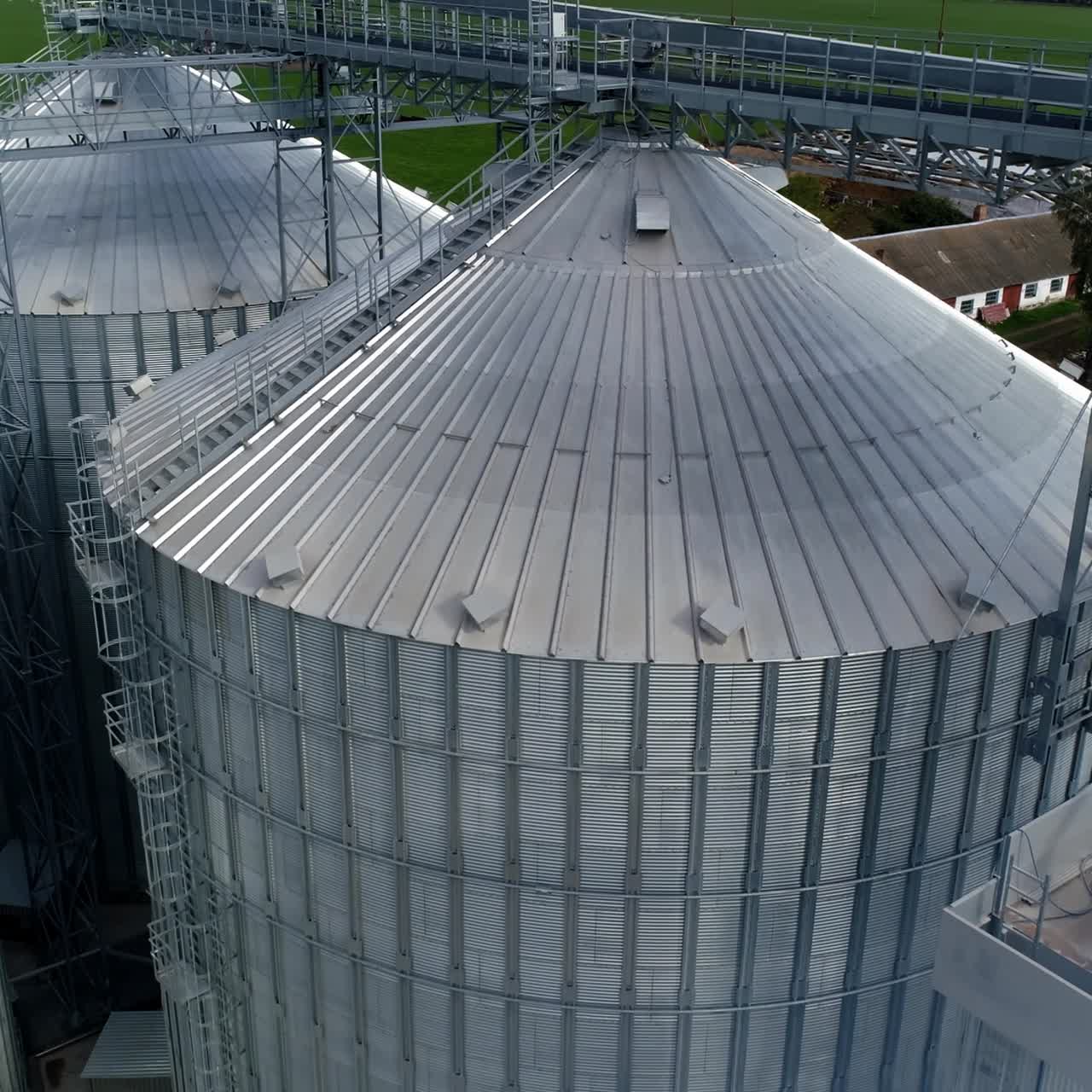 Grain elevators on field. Large metal granaries in smoke. Silver aluminum containers of a modern industrial plant. Aerial view