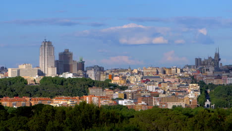 madrid’s skyline rises through rich layers of trees and rooftops, beneath a wide sky filled with billowing white clouds.