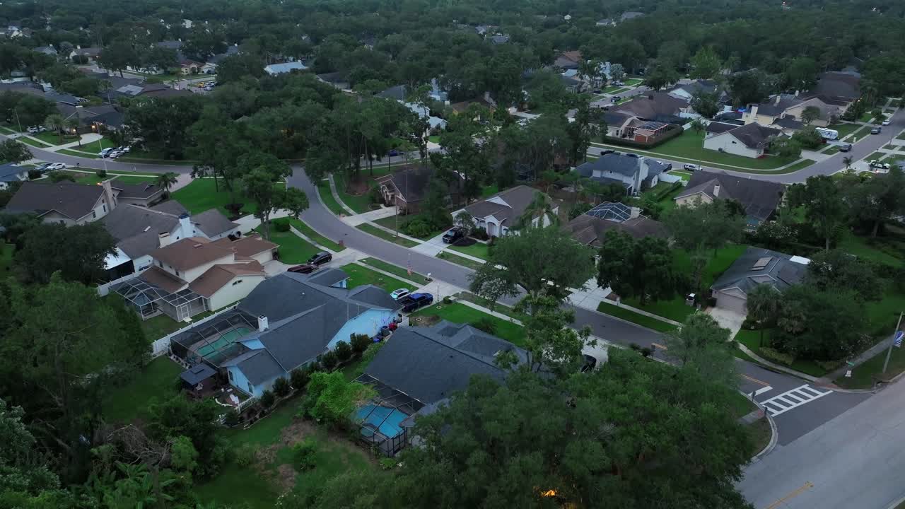 Luxury mansions in Florida suburb at dusk. Descend drone shot. Exclusive villas with transparent indoor swimming pool. Quiet neighborhood