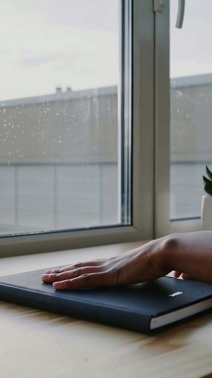 Vertical video: Picking up hands smoothing notebook at desk with tablet by window