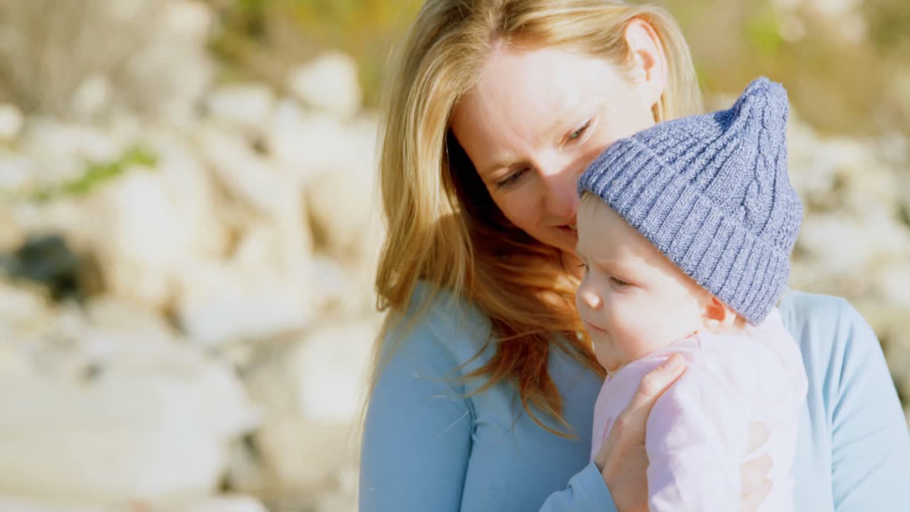 Vorderansicht einer kaukasischen Mutter mittleren Alters, die an einem sonnigen Tag am Strand ihr Baby ansieht 4k
