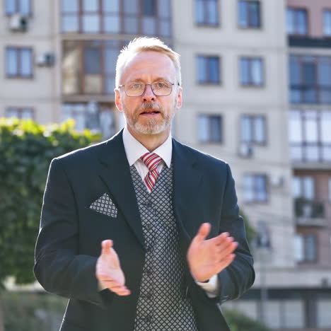 mature businessman telling something on the camera outdoors. portrait of a middle aged man in suit and tie talking in the street gesticulating a lot.