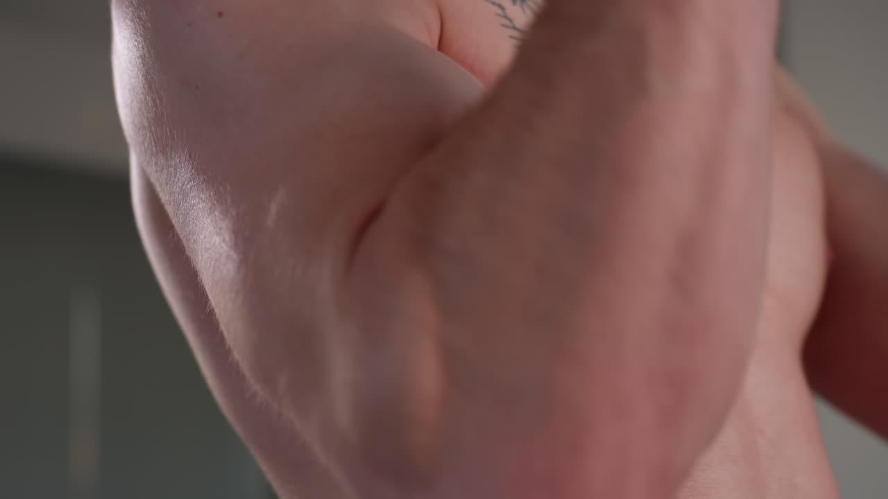 close up of fair skinned man's flexed arm as he pulls resistance rope during workout, focus on skin tone, muscular detail, and strength with soft blurred background inside light-colored space