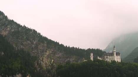 aerial dolly in of dramatic neuschwanstein castle on a hillside surrounded by a dense green pine forest on a foggy overcast day, bavaria, germany