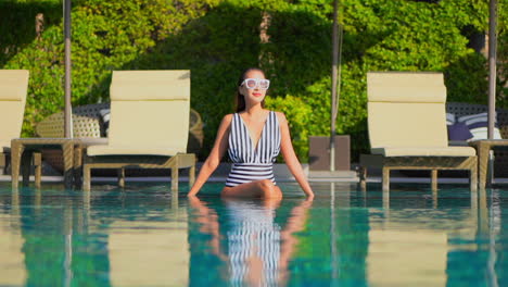 elegant asian woman with black and white swimsuit sitting in pool water