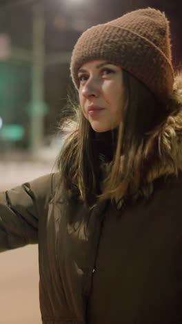 vista en primera persona de una mujer en un abrigo de invierno con una capucha de piel, estirando su mano por la noche con los autobuses que pasan