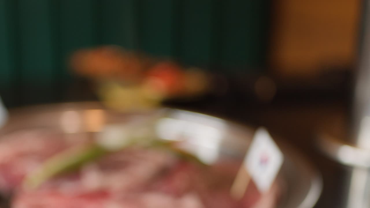 Out-of-focus shot of raw meat and vegetables on grill pan in warmly lit restaurant setting