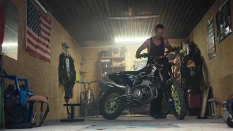a male mechanic rolls out his motorcycle from his workshop garage with numerous tools and a us flag. completion of repairs and test drive of the new bike