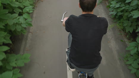 back view of someone cycling along a paved road with white markings, surrounded by lush roadside greenery, the cyclist pedals off, enjoying the scenic ride along the natural path