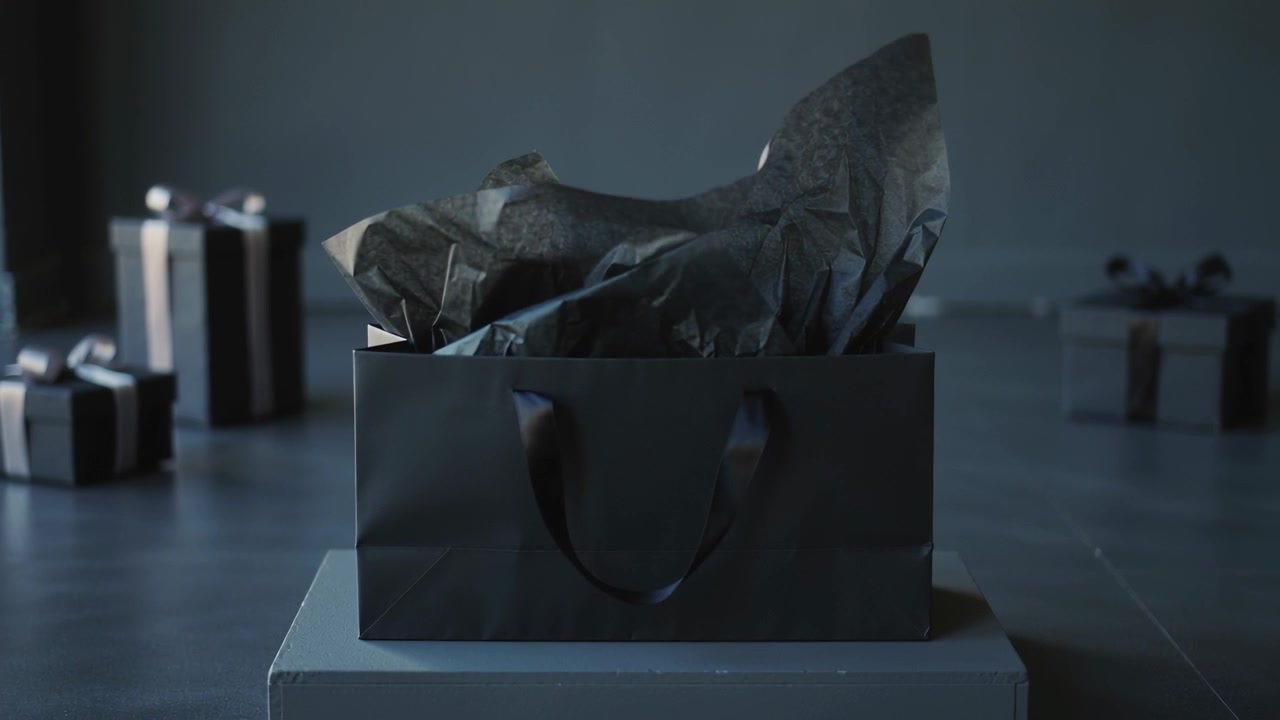 Carta velina che si dispiega all'interno di una borsa regalo nera opaca che si solleva su un piedistallo in studio, con regali incartati