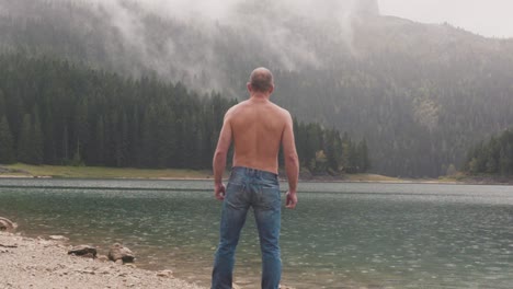 hombre de pie junto a un lago en un paisaje montañoso de niebla