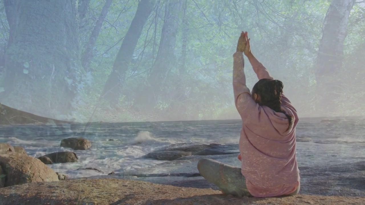 Vertical video: Breeze urging woman in hoodie, braid doing yoga on rocks, tree overlay, copy space