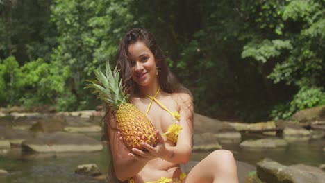 in the caribbean, two girls in bikinis have fun eating pineapple and relish a tropical waterfall and river.
