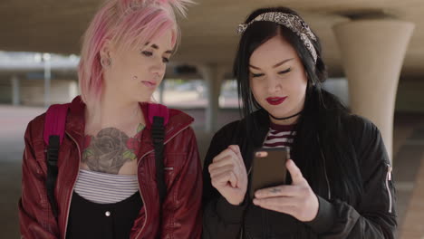 happy portrait of two authentic woman friends wearing alternative grunge fashion using smartphone browsing chatting