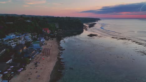 Drone-shot-of-a-beautiful-pink-sunset-over-Bingin-beach,-Bali,-at-low-tide