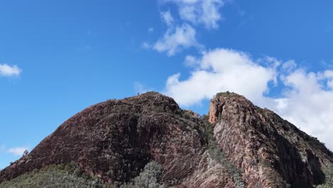 camera slowly pans across split rock’s rugged summit under bright daylight, revealing rocky textures, sparse vegetation, and a vivid blue sky with scattered clouds