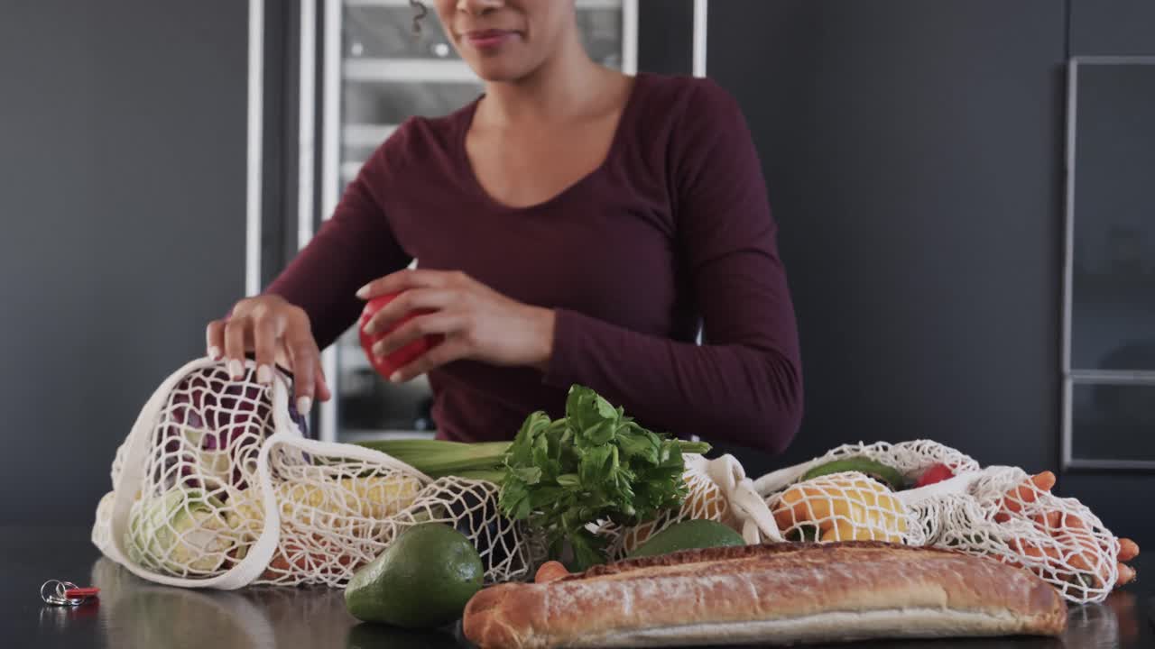 Midsection of biracial woman unpacking bags of grocery shopping in kitchen, in slow motion