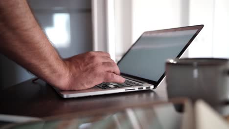 primer plano de las manos de un hombre escribiendo en una computadora portátil mientras trabaja desde casa