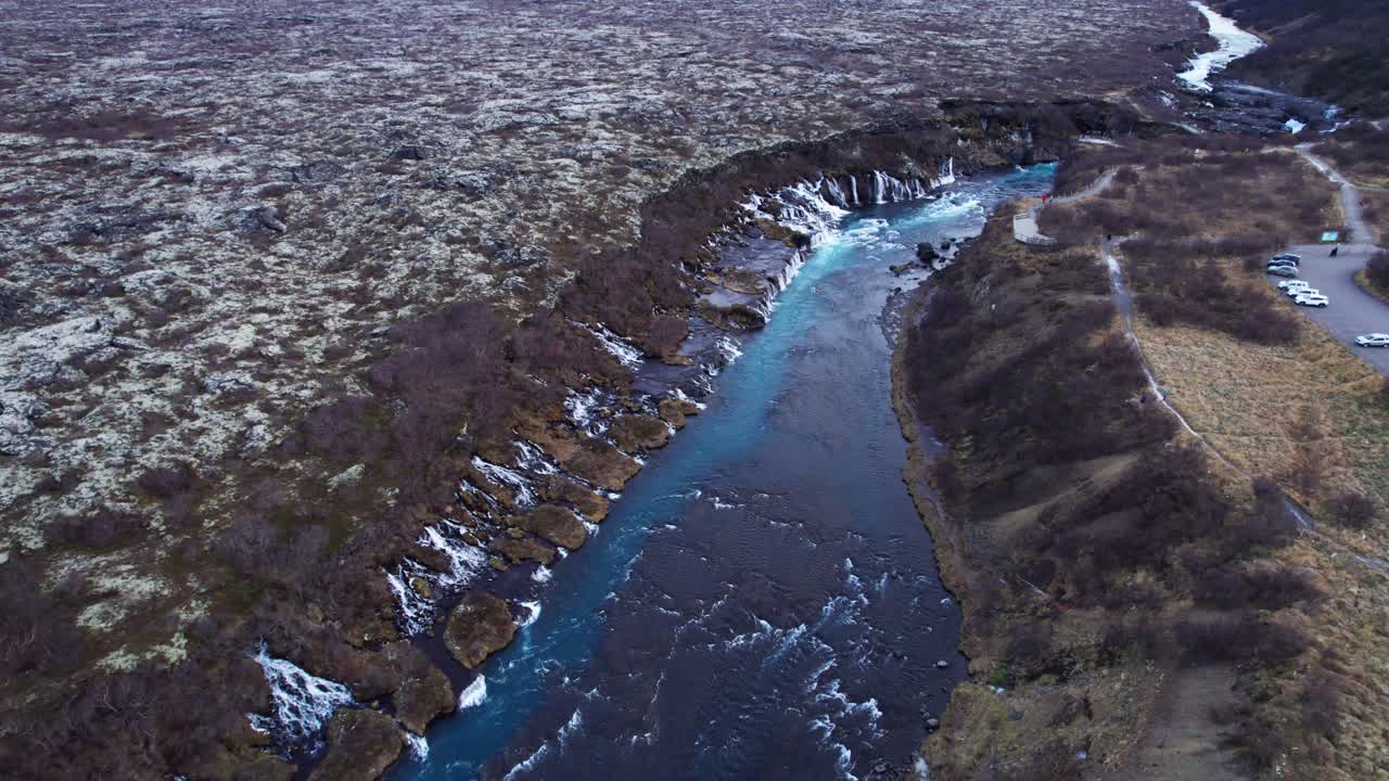 impresionante toma de drone de la cascada de hraunfossar y el río azul en un vasto paisaje volcánico
