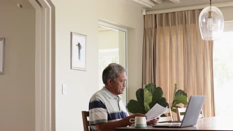 Biracial-älterer-Mann-Erledigt-Papierkram-Und-Benutzt-Laptop-Zu-Hause,-Zeitlupe