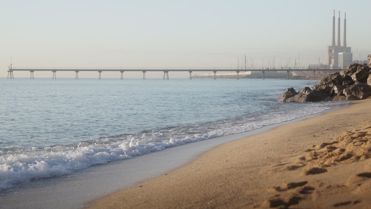 Slow motion waves on beach with industrial pier and factory in background
