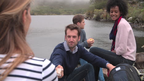 four friends on a walk taking a break by the edge of a lake