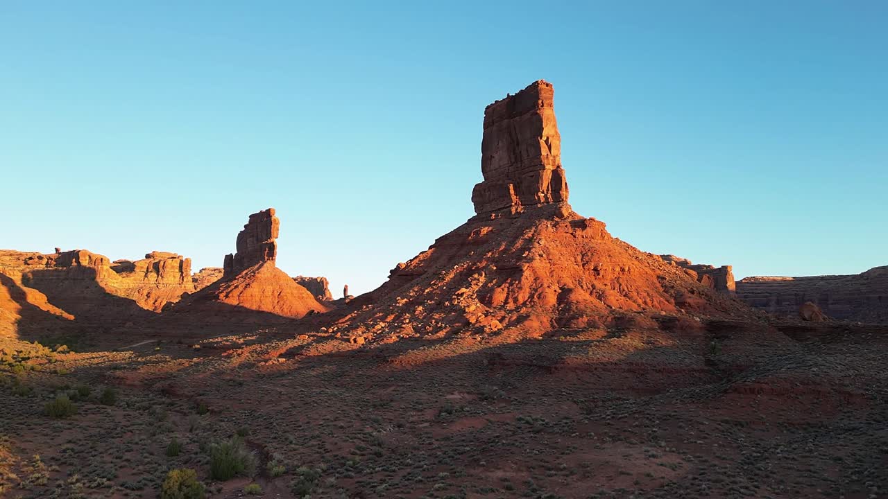 Sunrise drone hyperlapse with dolly movement showing Castle Butte and Stagecoach Rock in Valley of the Gods Utah USA. The rising sun progressively illuminates red rock formations under clear sky