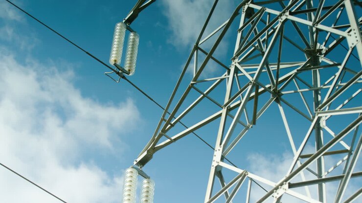 Clouds pass in blue sky over electrical pylon, low angle