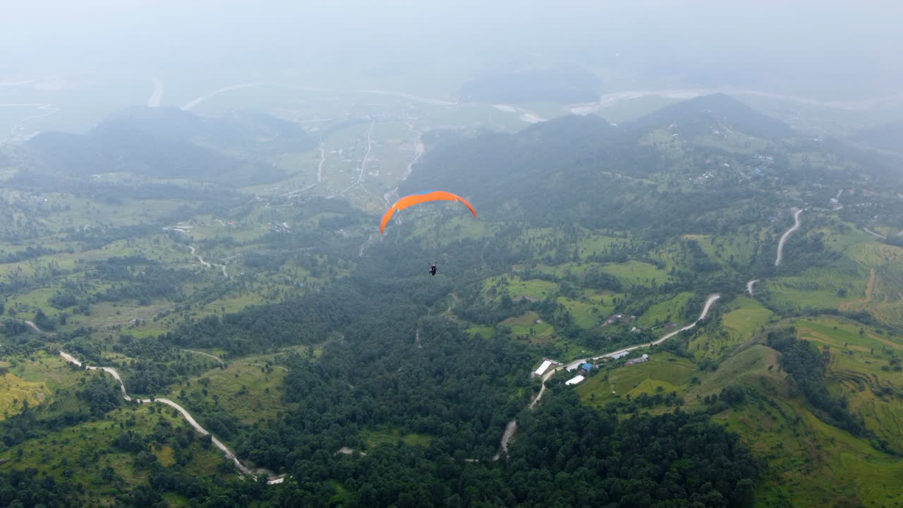Paraglider paira com asa de nylon laranja sobre um belo vale verde exuberante com nuvens e névoa