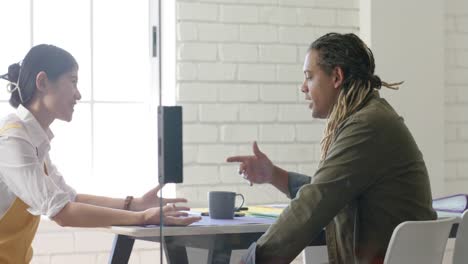 two diverse designers in discussion at table in casual creative meeting, in slow motion