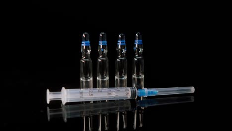 close-up of syringe and ampoules with vaccine against coronavirus. showing sample of medicine on black background, vaccination against covid-19, laboratory research concept