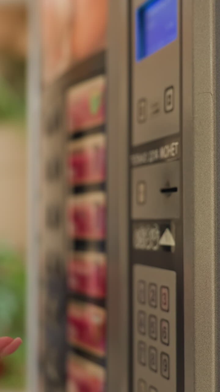 Close-up shot of businesswoman&#039;s hand inserting money into vending machine in office, preparing to buy snack during workday, showing focus on detail and casual moment in corporate setting