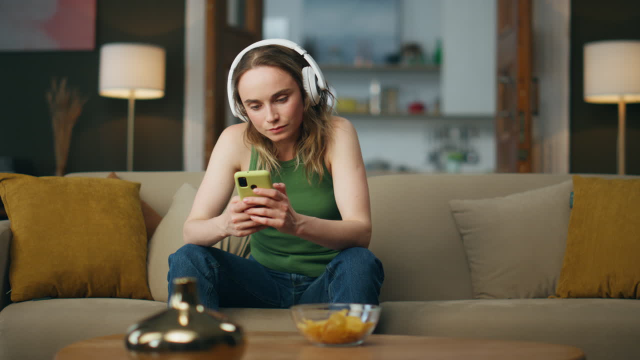 Donna con le cuffie che guarda il telefono a casa. Studente che ascolta un podcast educativo