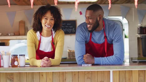 Retrato-De-Una-Pareja-Afroamericana-Con-Delantal-Sonriendo-Mientras-Está-De-Pie-En-El-Camión-De-Comida