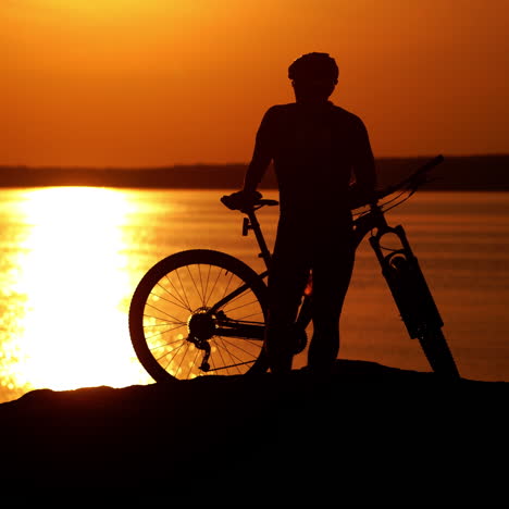 modern bicycle on the background of the beautiful sunset. bike near the river and the silhouette of a man wearing helmet and sport clothing in the evening.