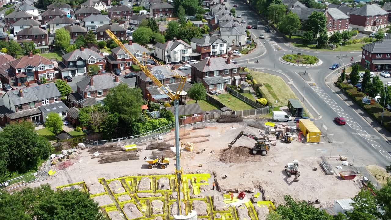 Tall crane setting building foundation in British town neighbourhood aerial pull back view above suburban townhouse rooftops