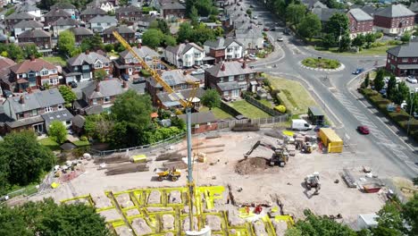 Tall-crane-setting-building-foundation-in-British-town-neighbourhood-aerial-pull-back-view-above-suburban-townhouse-rooftops