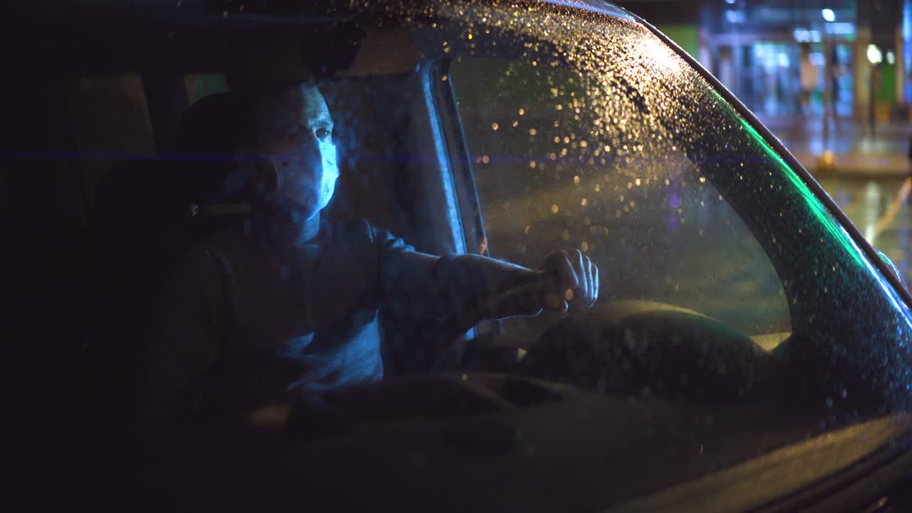 비가 오는 저녁에 차에 앉아 있는 의료 마스크를 입은 젊은 남자