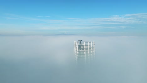 in aerial video, the drone orbits right, encircling a solitary skyscraper amid thick morning clouds on the left