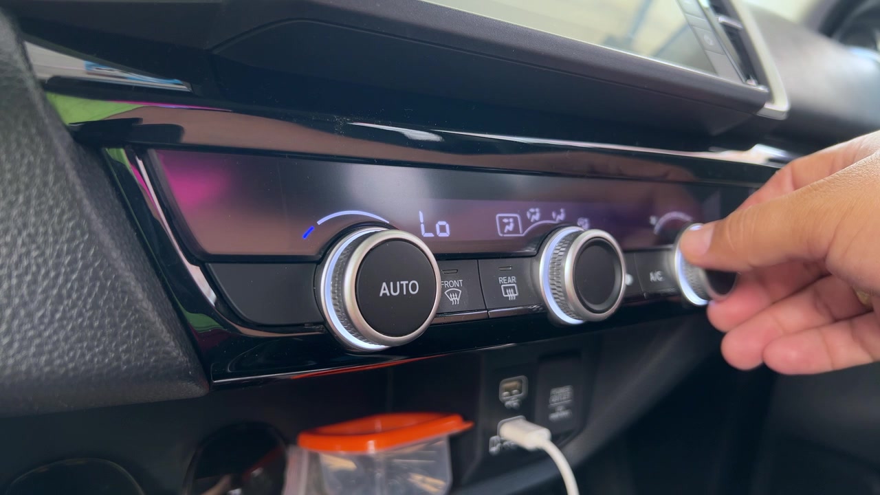 Close-up de pessoa ajustando o botão do controle de climatização no painel de um carro moderno com configurações de temperatura, tecnologia automotiva e interior do veículo