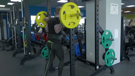 man performing barbell back squat in a gym