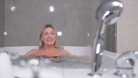 portrait of a smiling blonde woman taking a hot bath with warm bubbles. health procedures in the spa salon.