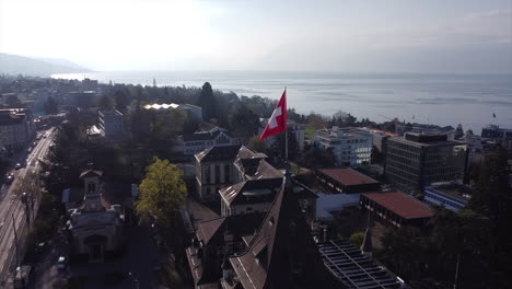 slow aerial descent shot of the swiss flag on top of a renaissance building in lausanne, switzerland on a sunny day