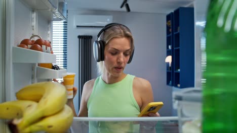 mujer en la cocina usando el teléfono y bebiendo yogur