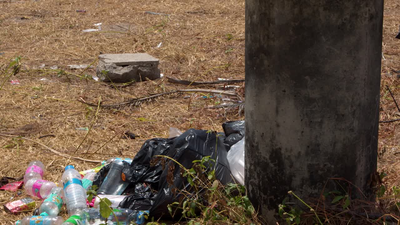 Inquadratura statica di bottiglie di plastica e sacchi neri della spazzatura ammucchiati su erba secca in Thailandia