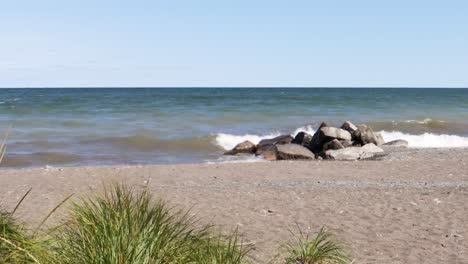 Gently-rolling-waves-crash-onto-a-group-of-rocks-on-a-sandy-beach-on-a-sunny-day