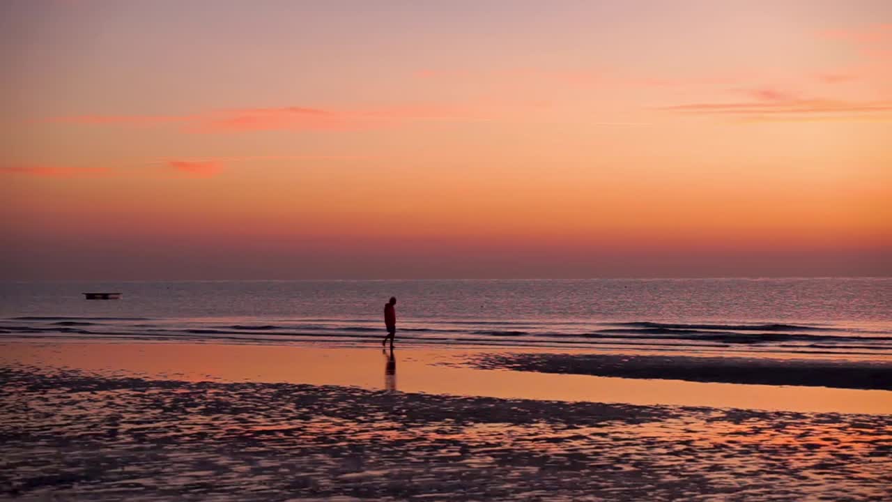 Male silhouette walking on the sore during a low tide at sunrise (golden hour) and with a calm but slightly wavy sea