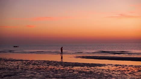 male silhouette walking on the sore during a low tide at sunrise (golden hour) and with a calm but slightly wavy sea